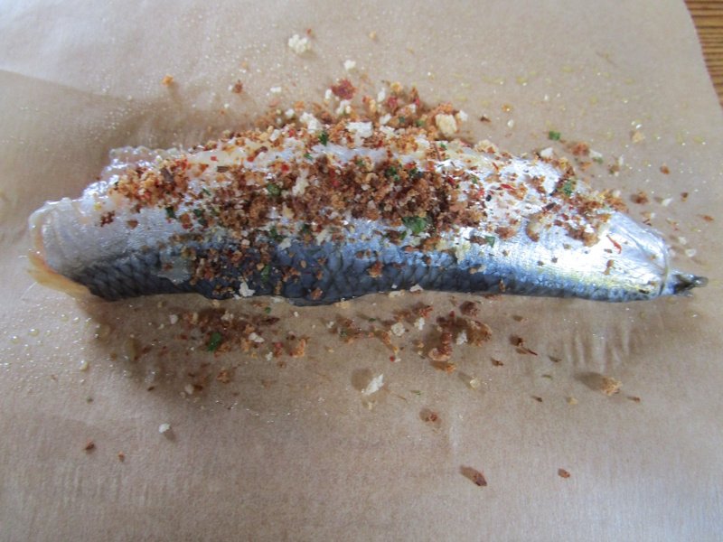 Seasoned and crumbed sardines lying on unbleached paper before folding to make the box.