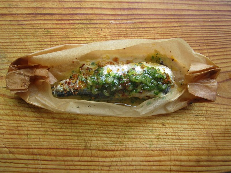 A roasted sardine with parsleyed breadcrumbs baked in a paper box.